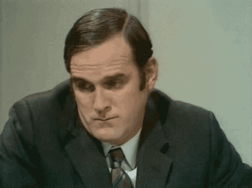 a man in a suit and tie is sitting at a table making a face .