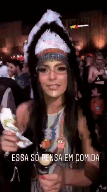 a woman in a native american costume is holding a packet of food with the words essa so pensa em comida written below her
