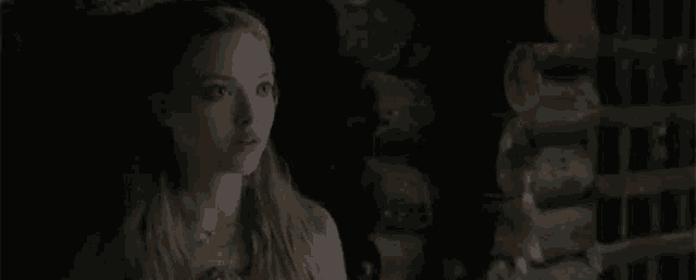 a young woman is standing in a dark room next to a log wall .