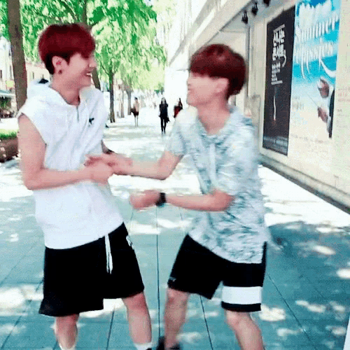 two young men are hugging each other on a sidewalk in front of a building with a sign that says summer