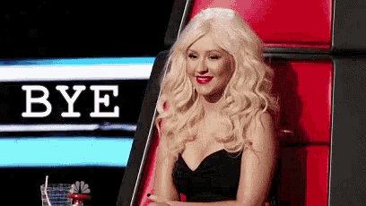 a blonde woman in a black dress is sitting in a chair with the word bye behind her .