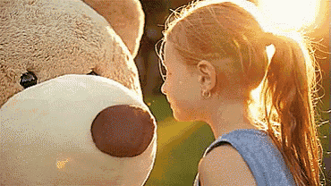 a little girl is standing next to a large teddy bear and looking at it .