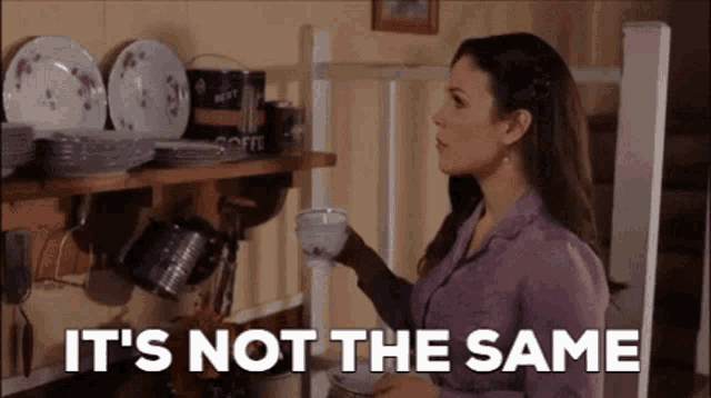 a woman in a purple shirt is holding a cup of coffee in a kitchen .