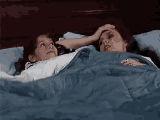 two women are laying in a bed with a blue blanket