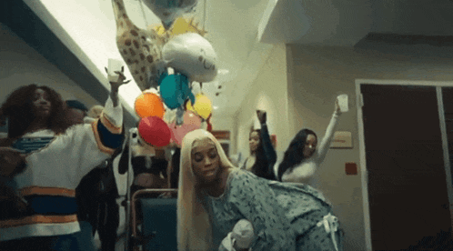 a woman in a hospital gown is holding balloons and a baby