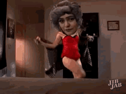 a woman in a red corset is dancing in front of a mirror in a room .