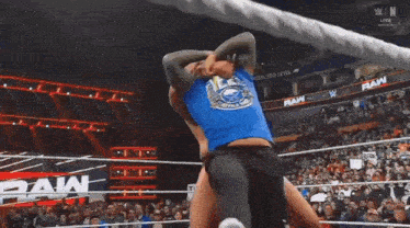 a man in a blue shirt is wrestling another man in a ring .