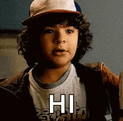 a young boy with curly hair is wearing a hat and a t-shirt that says hi .