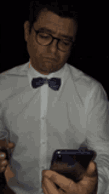 a man wearing glasses and a bow tie looks at his phone