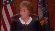a female judge is sitting at a desk with an american flag in the background