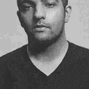 a black and white photo of a man with a beard wearing a v-neck t-shirt .