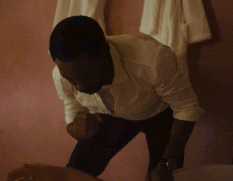 a man in a white shirt stands in front of a pink wall with white towels hanging on it