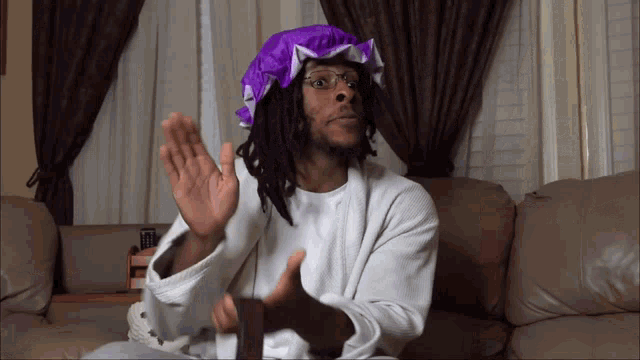 a man with dreadlocks is wearing a white robe and a purple cap