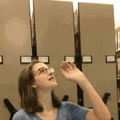 a woman wearing glasses is standing in front of a row of filing cabinets ..