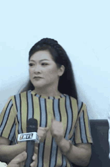 a woman in a striped shirt is holding a microphone and talking into it .