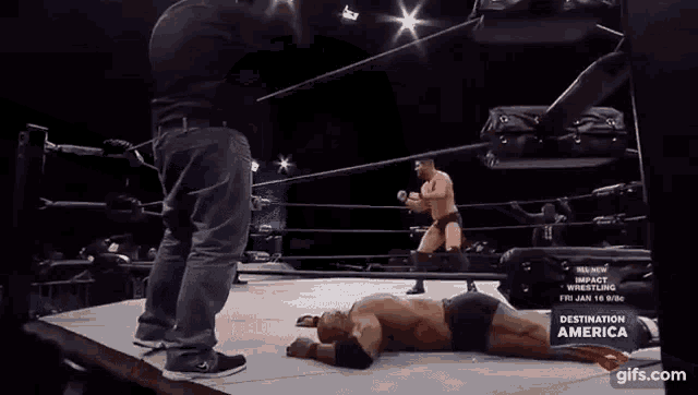 a wrestler is laying on the ground in a wrestling ring while another wrestler stands behind him .