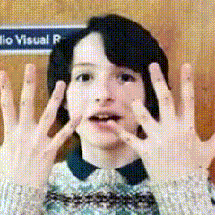 a woman making a funny face with her hands in front of a sign that says visual r.