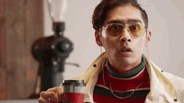 a man wearing sunglasses is holding a cup of coffee that says ' caffeine ' on it