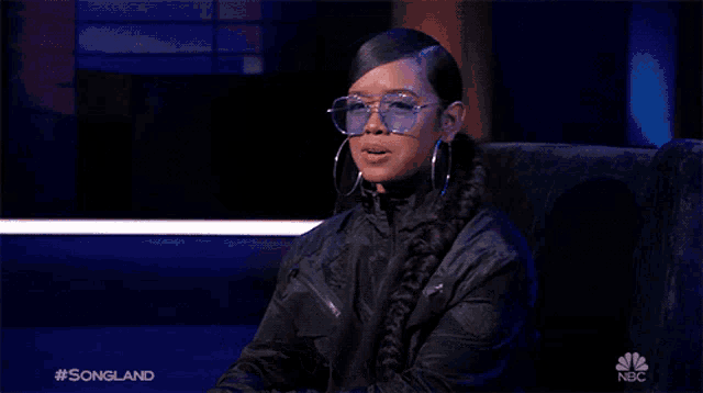 a woman wearing glasses and hoop earrings is sitting in a chair on nbc 's songland