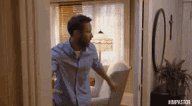 a man in a blue shirt is walking into a living room .