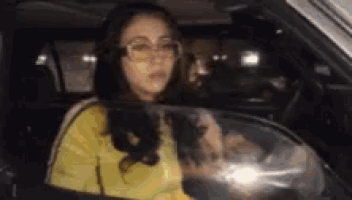 a woman wearing glasses is sitting in the driver 's seat of a car at night .