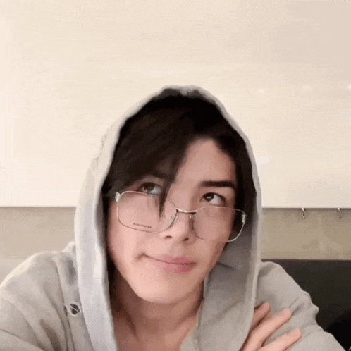 a young man wearing glasses and a hoodie is looking at the camera and smiling .