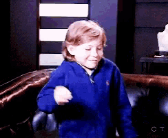 a young boy wearing a blue jacket is dancing in a living room .