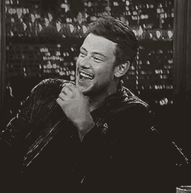 a black and white photo of a man laughing with his hand on his mouth .