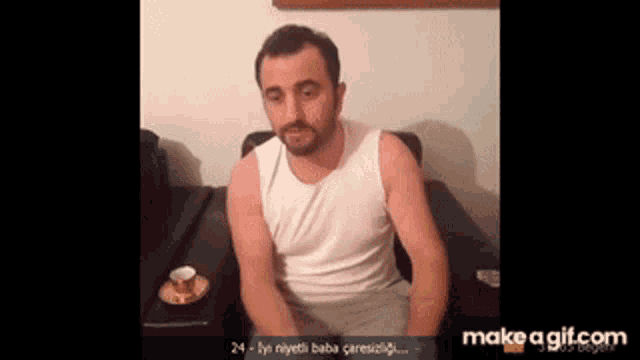 a man in a white tank top is sitting at a table with a cup on it .