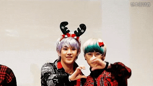 two young men are making a heart shape with their hands while wearing reindeer horns .