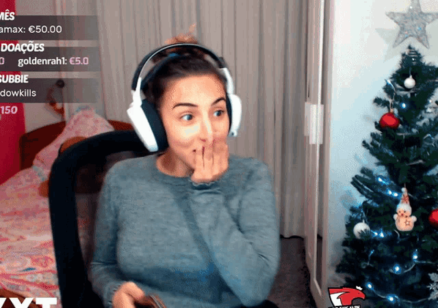 a woman wearing headphones is covering her mouth in front of a christmas tree
