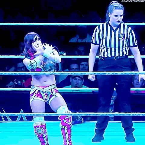 a female wrestler is standing in a wrestling ring with a referee .