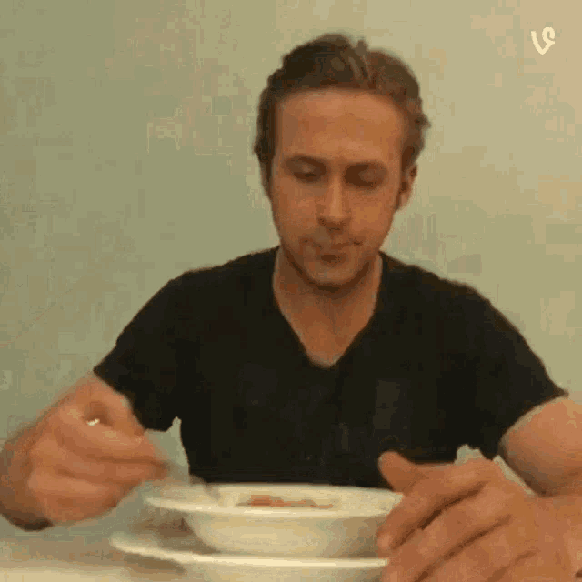 a man in a black shirt is sitting at a table eating a bowl of soup .