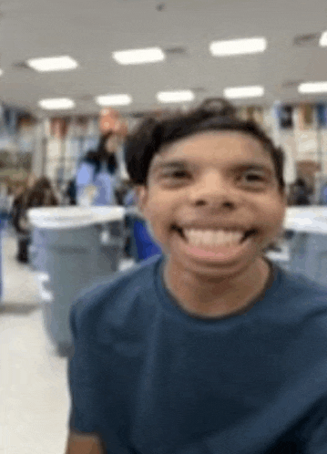 a man in a blue shirt is smiling and making a funny face in a room .