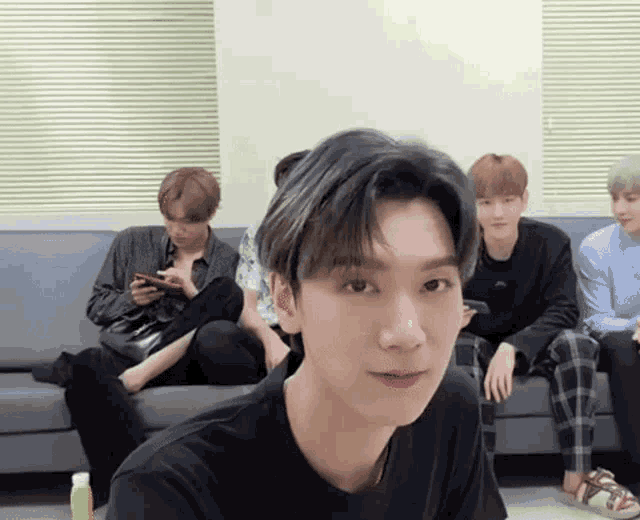 a group of young men are sitting on a couch and one of them is wearing a black shirt .