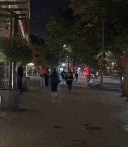 a group of people walking down a street at night with a bus stop in the background
