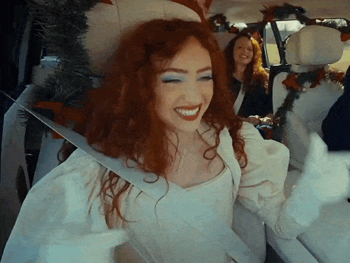 a woman with red hair is smiling while wearing a white dress