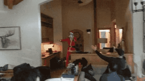 a man in a santa suit stands in a living room with his arms outstretched
