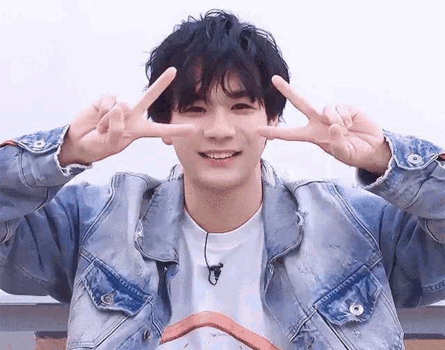 a young man in a denim jacket is making a peace sign with his hands