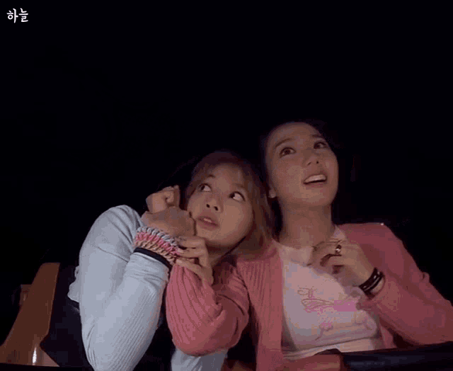 a couple of women sitting next to each other with a drawing of a crown in the background