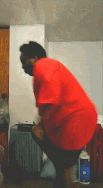 a man in a red shirt is squatting down next to a suitcase