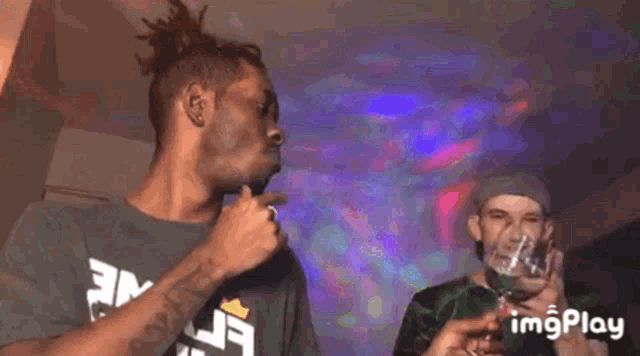 a man is holding a glass of wine in front of a microphone while another man looks on .