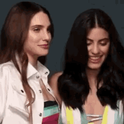 two women are standing next to each other and smiling . one of the women is wearing a striped dress .