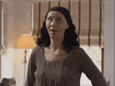 a woman wearing a headband and a brown shirt is standing in front of a lamp