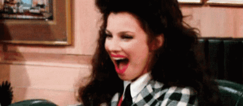 a woman in a plaid suit and tie is laughing with her mouth open .