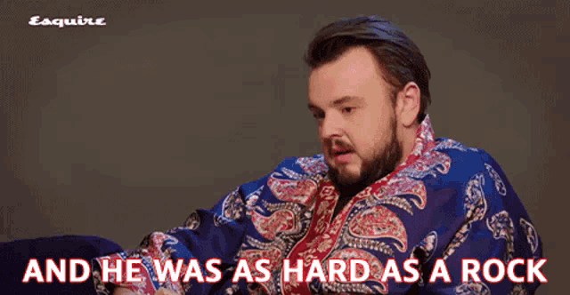 a man with a beard wearing a blue paisley shirt with the words " and he was as hard as a rock "