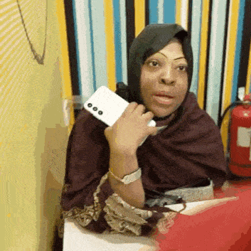 a woman in a hijab is sitting at a table talking on a cell phone .