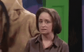 a woman is standing in front of a green door making a funny face .