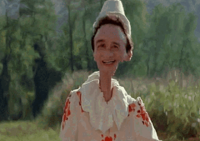 a clown with a very large head is smiling in a field with trees in the background .