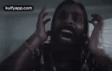 a man with a beard is screaming and holding his hands up in the air .